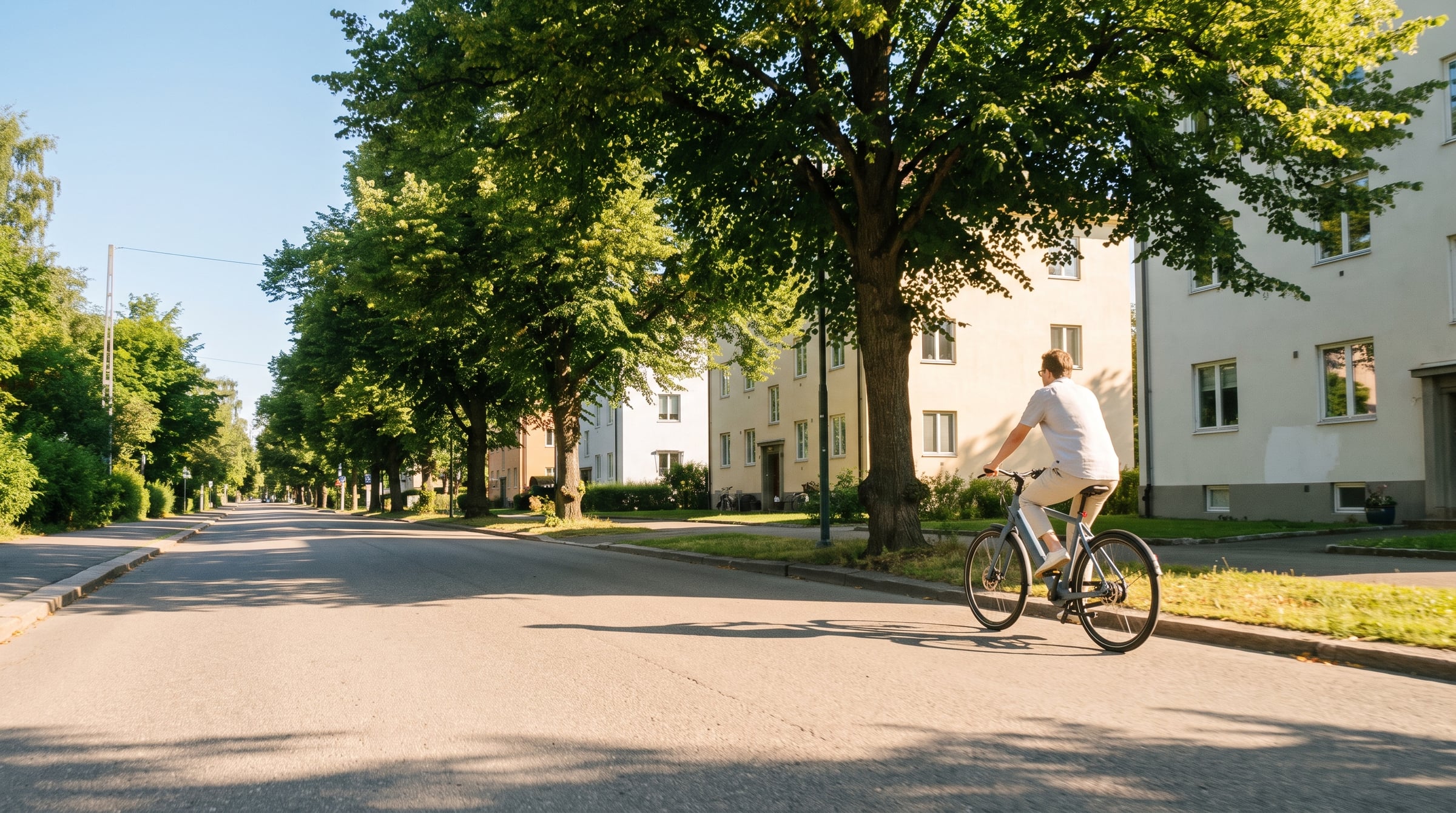 A rider on a Sykla City bike travelling down a quiet Oslo street on a bright overcast morning.